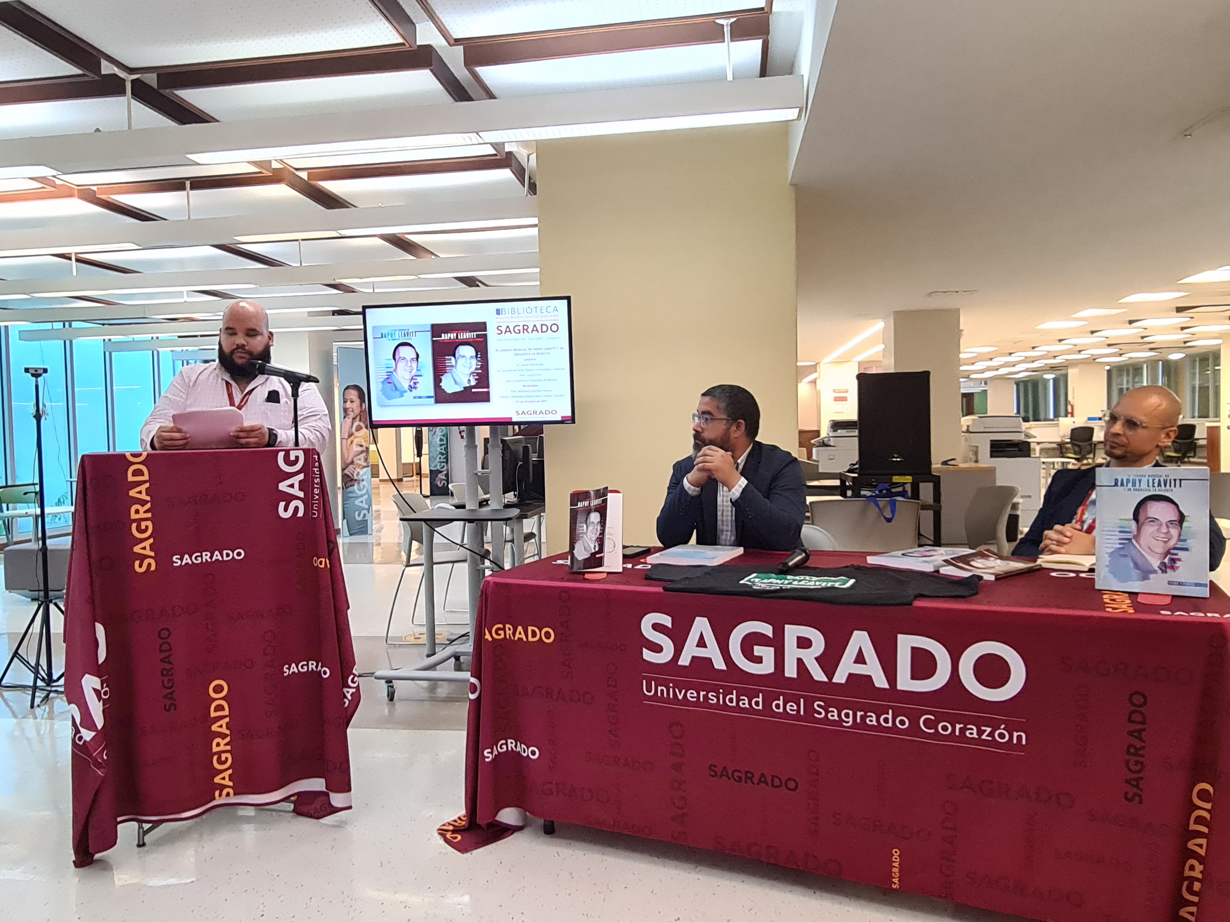 imagen de monderador en podia y lectores invitados sentados en mesa de discusion 