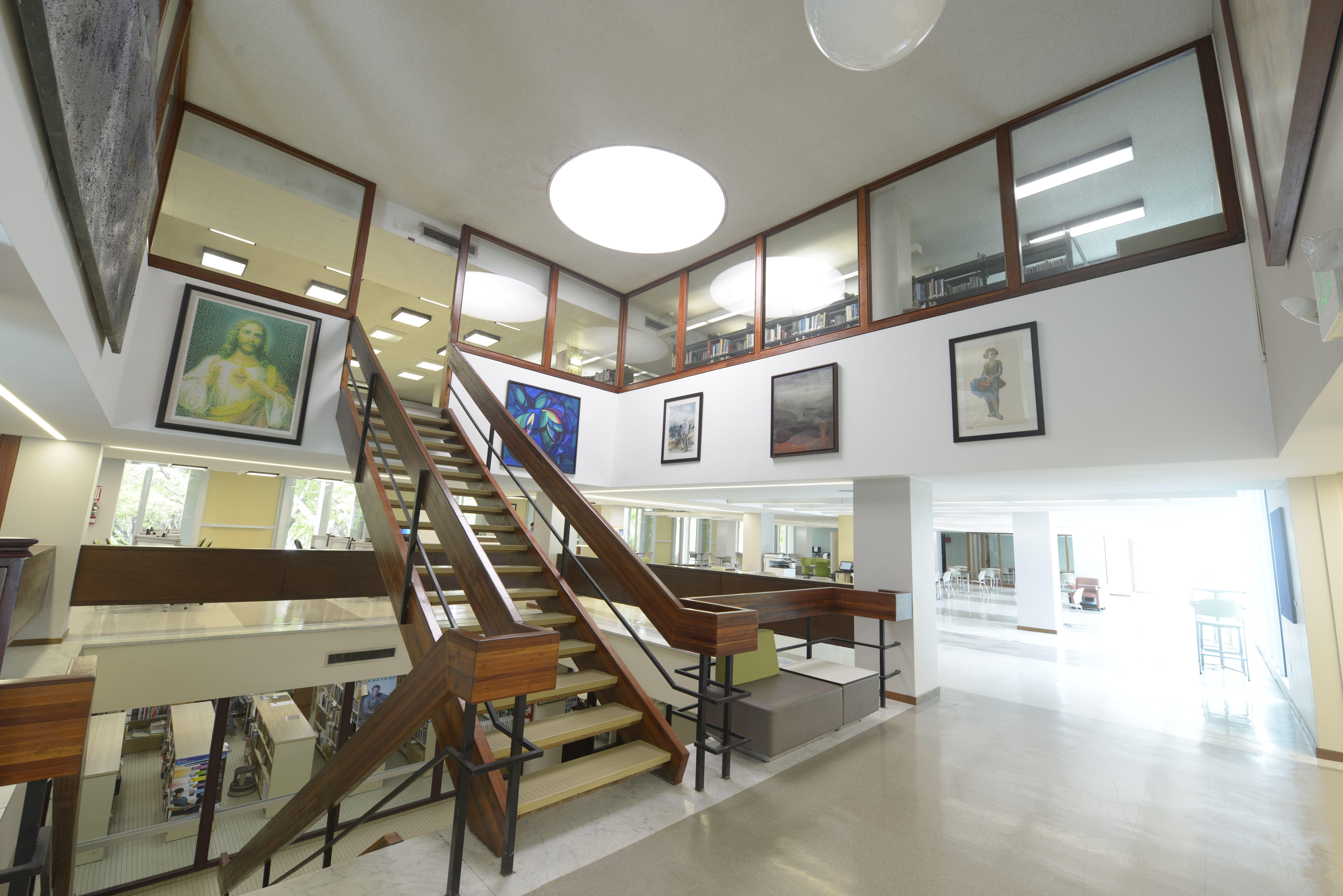 Fotografia del area de coleccion general desde una toma hacia su entrada, escaleras y anaqueles de libros